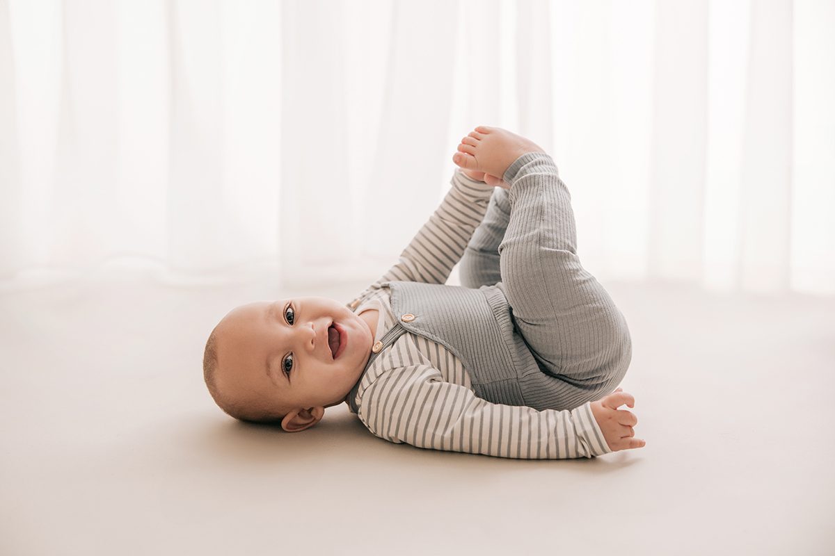 baby laughing holding his toes in front of a white sheer curtain