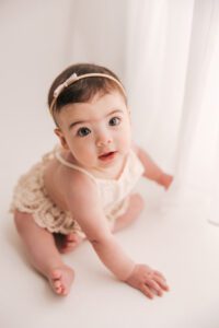 baby girl looking up at camera next to a curtain