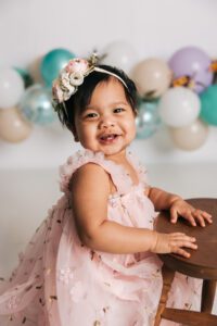 baby girl smiling in front of colorful teal and purple balloons