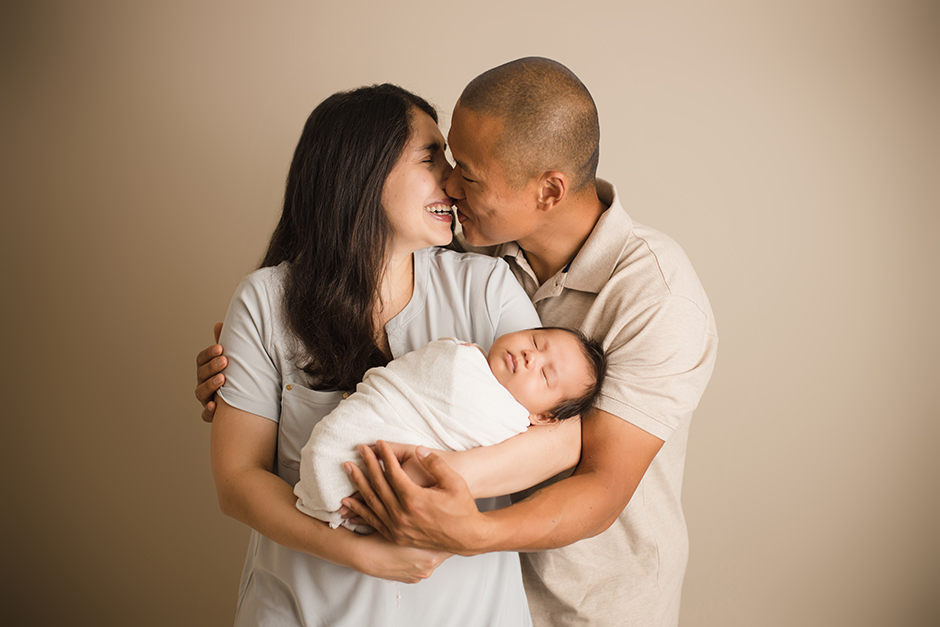 parents kissing holding newborn baby photo raleigh