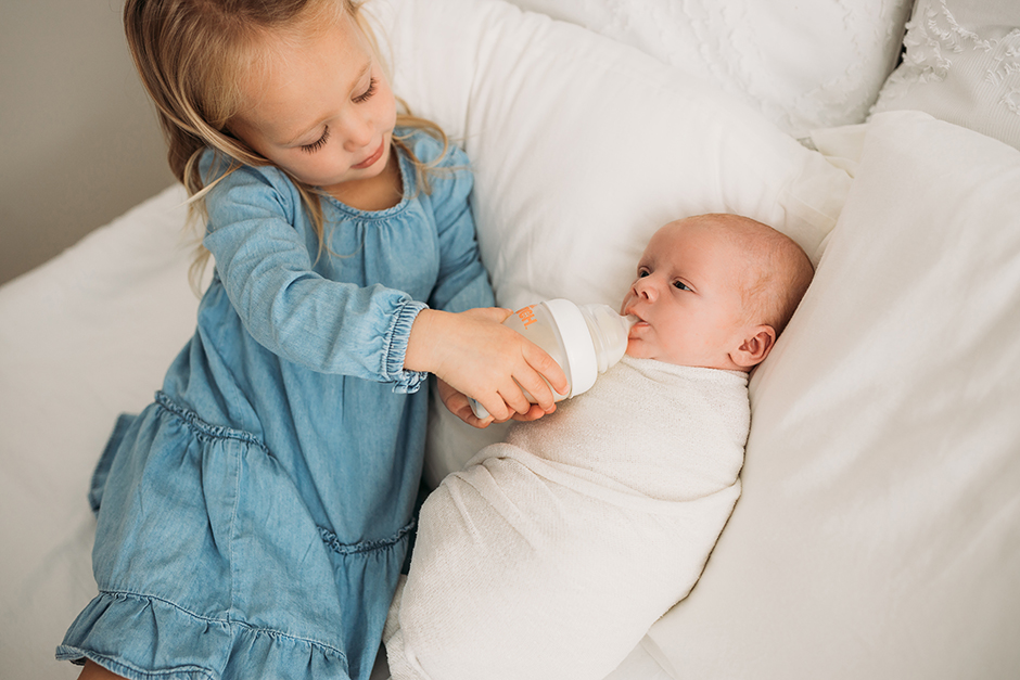 sister feeding baby in cary newborn studio