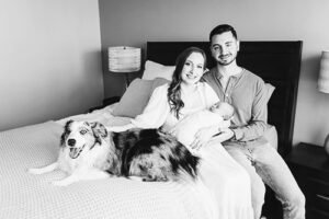 newborn and parents on bed with dog