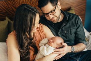 closeup of baby with parents sitting on bed- Raleigh Lifestyle Newborn Photographer