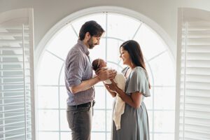mom and dad with baby in front of window