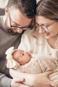 Happy new parents smile down at their awake newborn baby in mom's arms after visiting raleigh baby stores