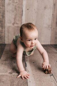 A toddler boy in green overalls plays with a wooden car on a studio floor from a toy store raleigh nc
