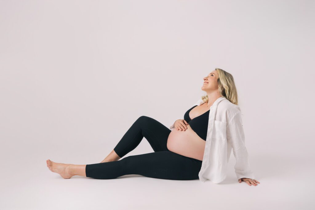 pregnant mom sitting on ground in leggings smiling