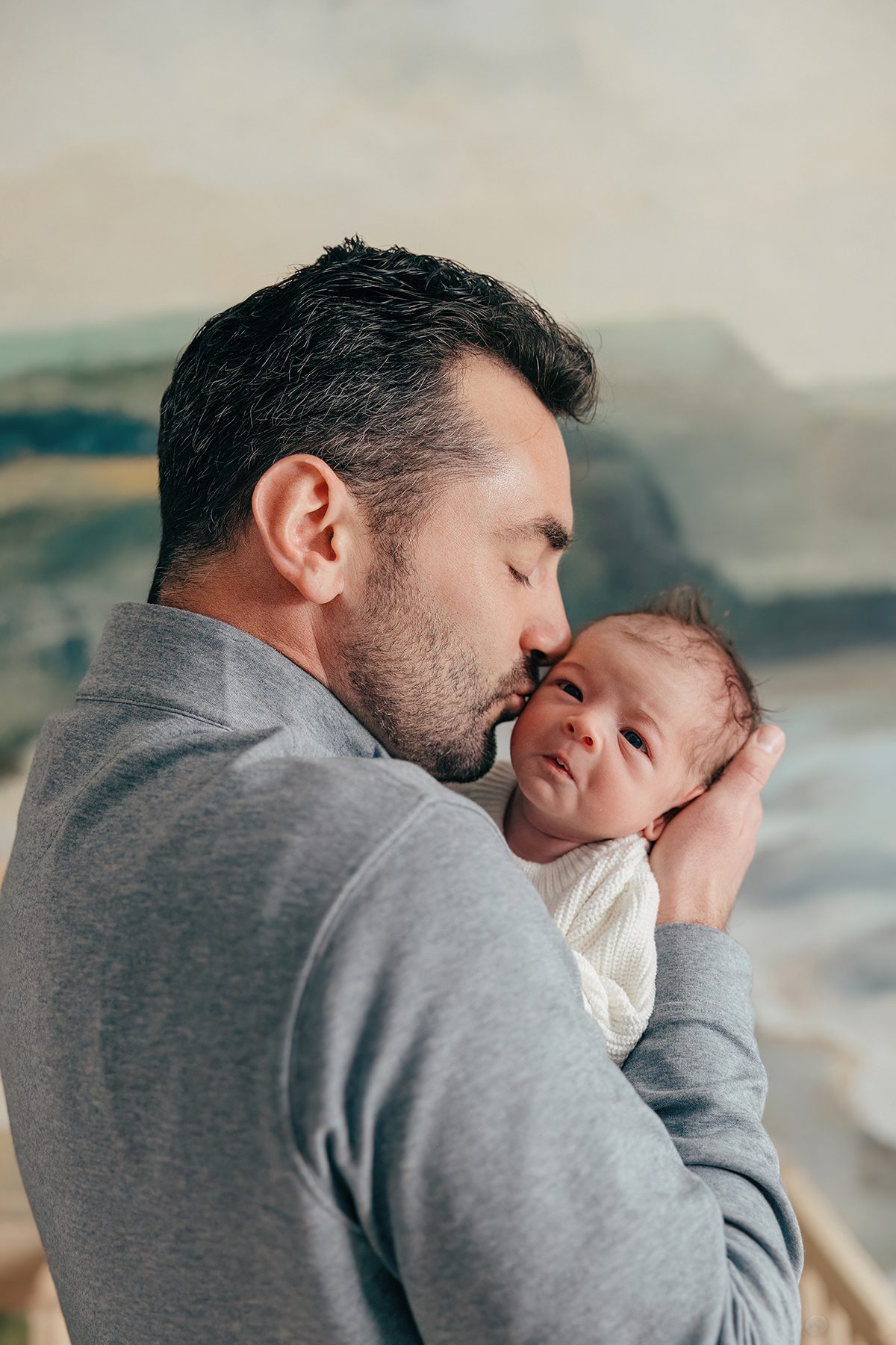 dad kissing newborn baby with mural wallpaper behind, cary in home photography