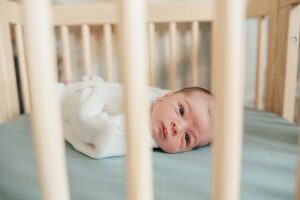 baby peeking through natural wood crib slats. cary in home photography