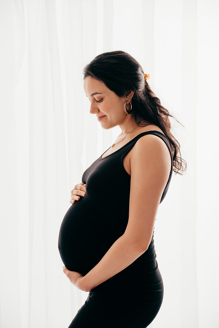 Silhouette of a pregnant mom in a black dress in front of a curtain, raleigh maternity photographer
