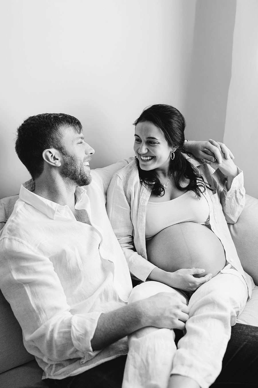 black and white photo of pregnant mom and dad laughing on couch, raleigh newborn photographer